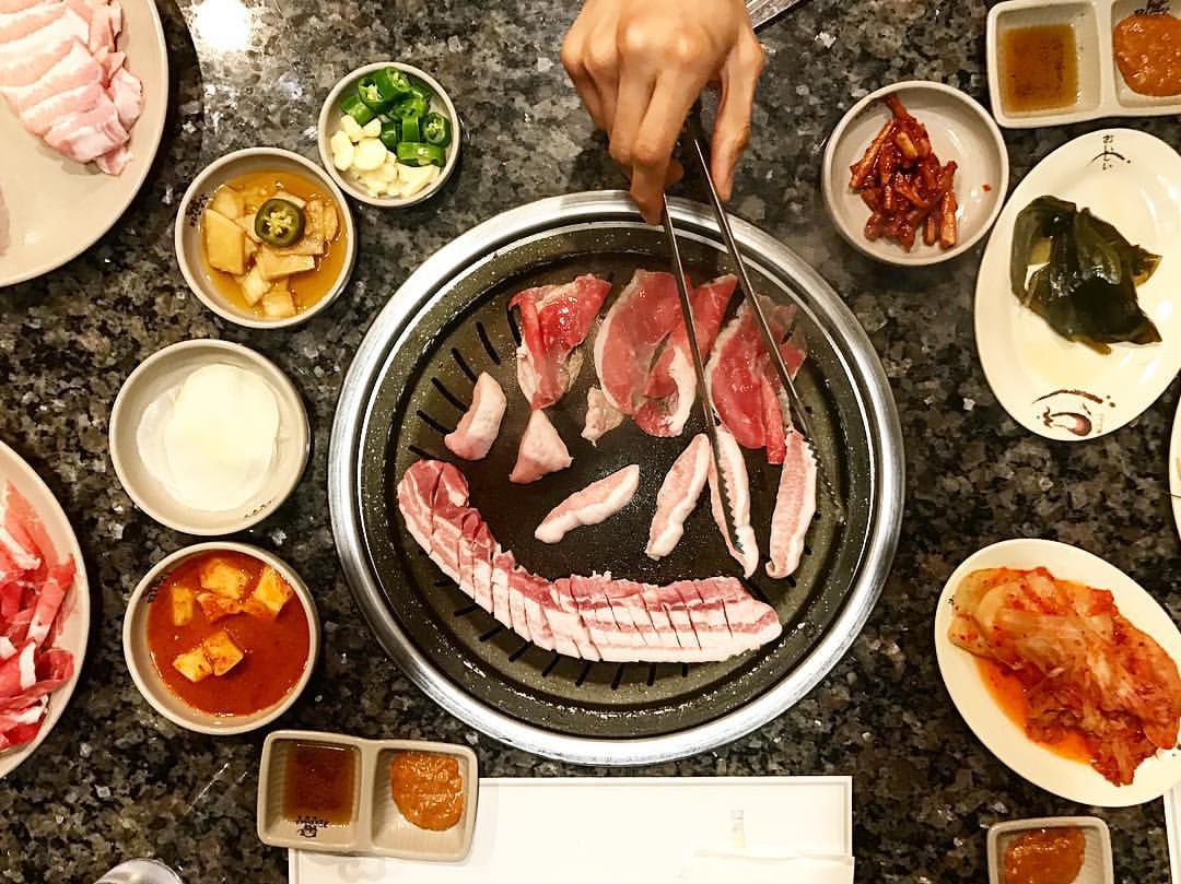 Pork cooking on a grill, surrounded by banchan.