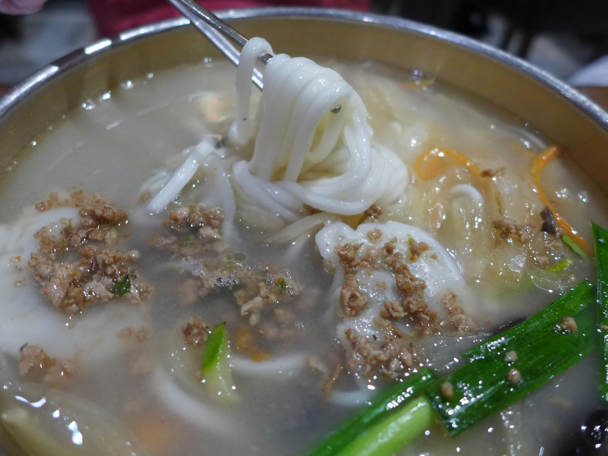 An opaque white broth with thick white held aloft by chopsticks.