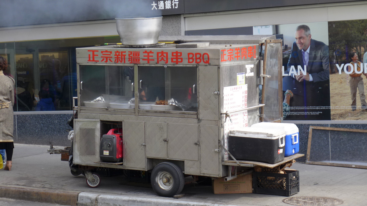 A metal food cart on the sidewalk with steam coming out the top