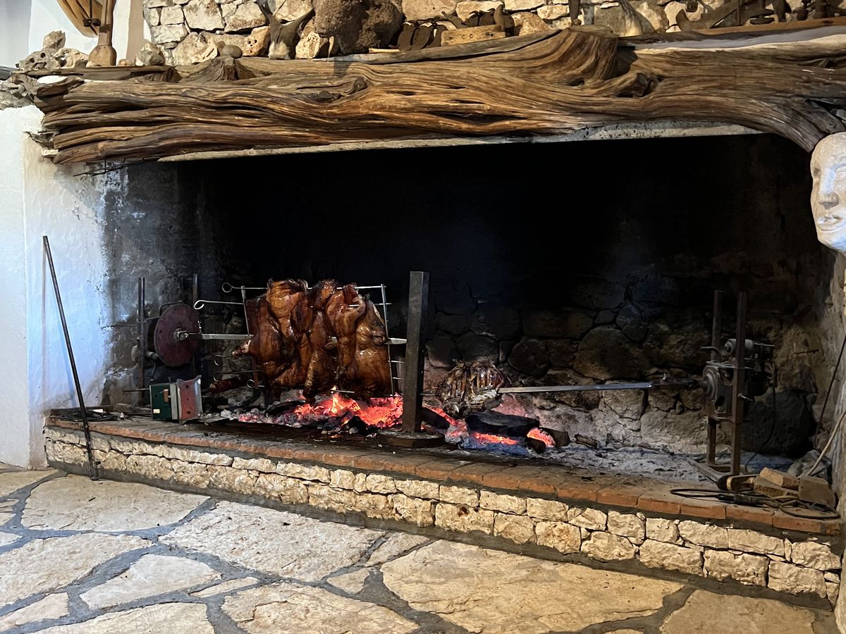 A large stone hearth where coals burn brightly and roasted meats sit on a rack.