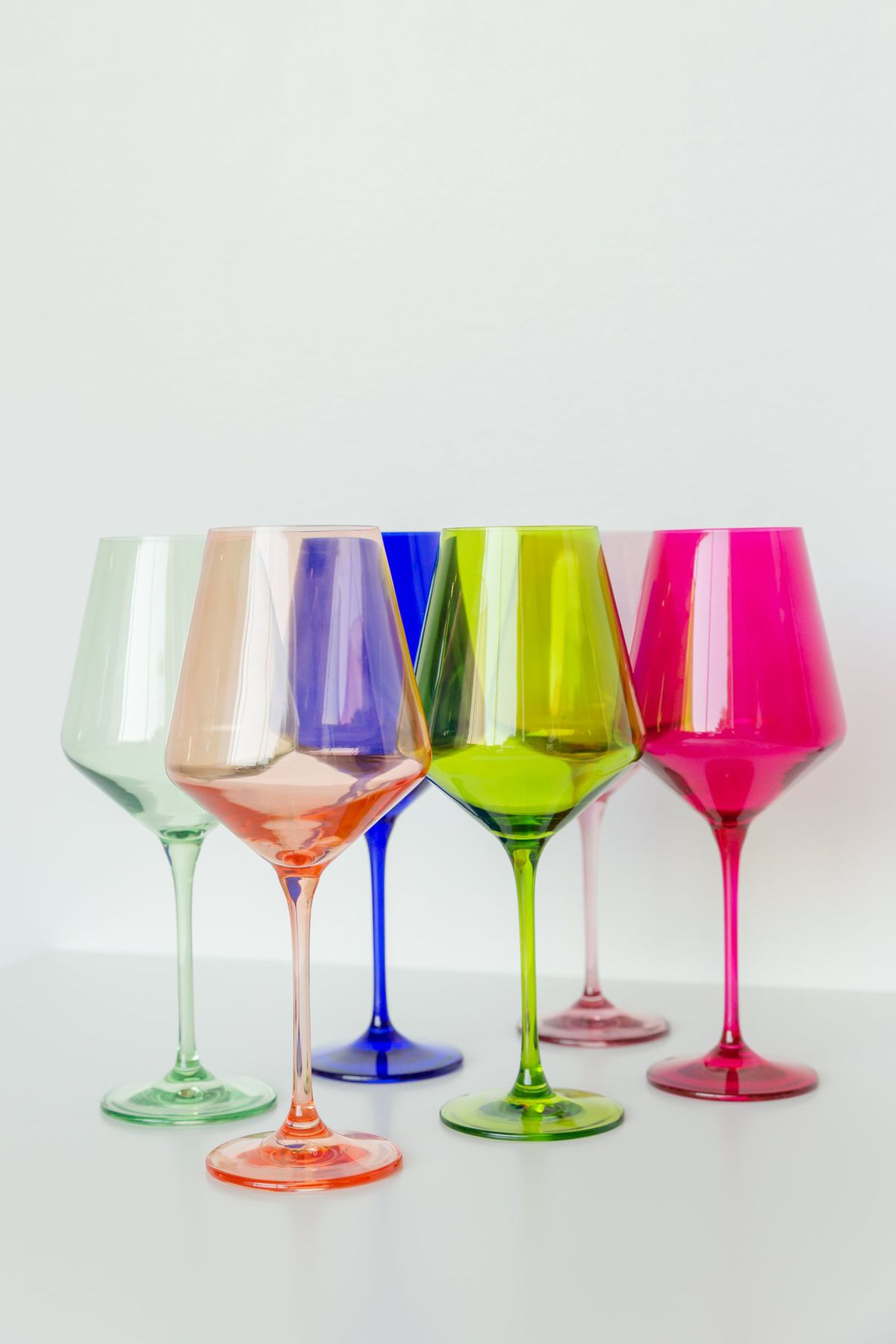 Six wine glasses in jewel tones of green, pink, blue, peach, fuchsia, and mint