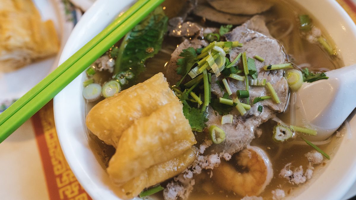 An overhead photo of a bowl of Cambodian soup with doughnuts and green chopsticks.