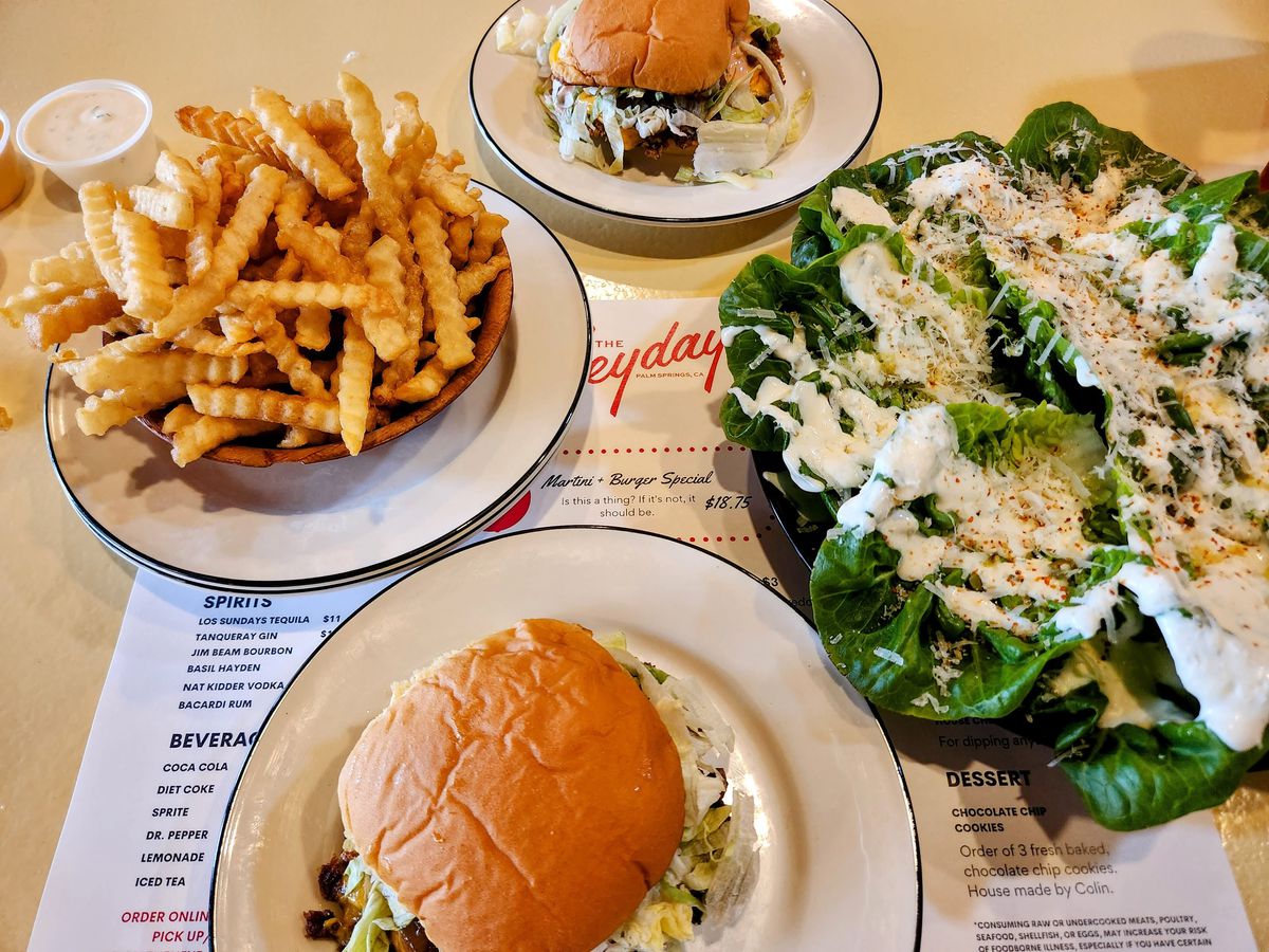 A tabletop scattered with fries, salad, and burgers at Heyday in Palm Springs.