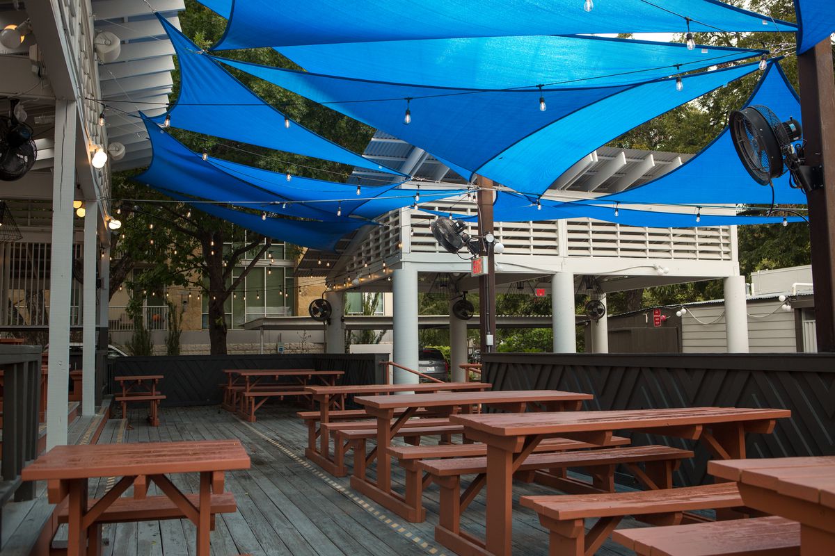 An outdoor dining space with picnic tables and hanging blue awnings.