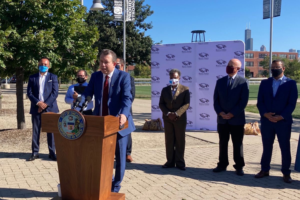 Newly announced Chicago Public Schools CEO Pedro Martinez, wearing a blue suit, stands outside at a lectern and speaks during a press conference as district leaders look on behind him.
