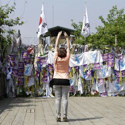 A visitor stands on their toes while taking souvenir photos in front of a wire fence covered with ribbons carrying messages left by visitors wishing for the reunification of the two Koreas, at the Imjingak Pavilion near the border village of Panmunjom, which has separated the two Koreas since the Korean War, in Paju, north of Seoul, South Korea, Sunday, June 9, 2013. Government delegates from North and South Korea began preparatory talks Sunday at Panmunjom, a "truce village" on their heavily armed border aimed at setting ground rules for a higher-level discussion on easing animosity and restoring stalled rapprochement projects. (AP Photo/Lee Jin-man)