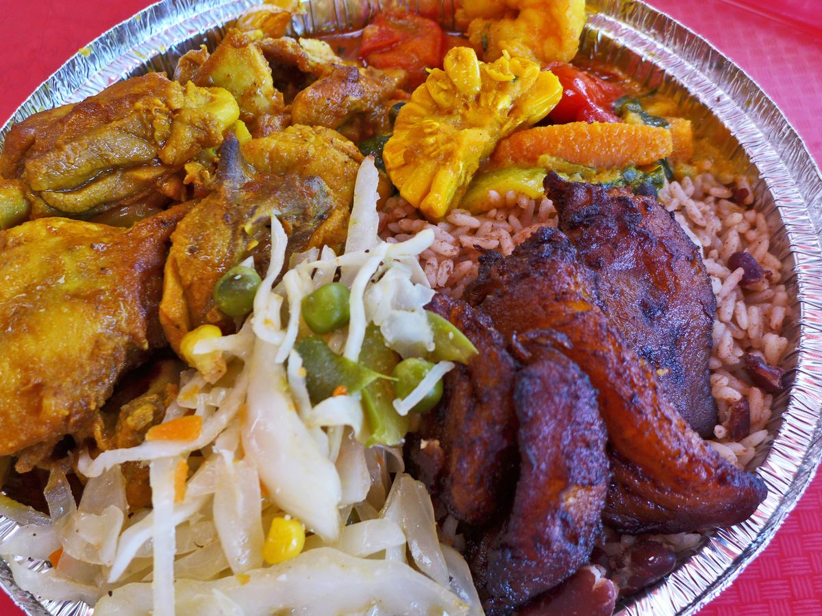 An aluminum container with chicken, corn, plantain, rice, and beans jumbled therein.