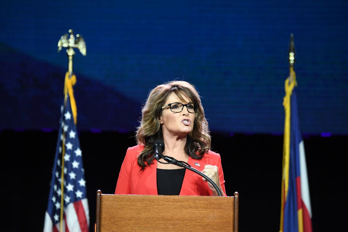A person, former Alaska Governor Sarah Palin, stands at a podium, flanked by two flags.