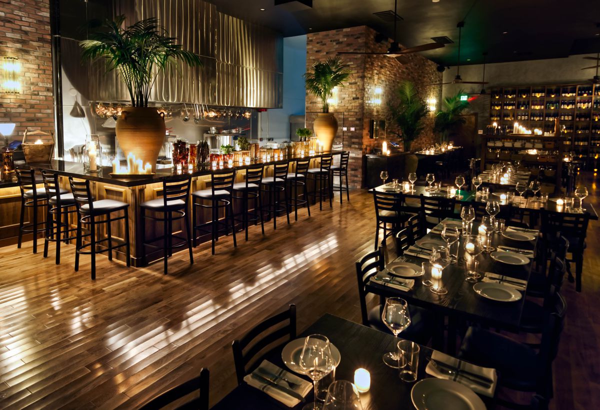 A corner bar and open tables with dark wood at a new Italian restaurant, at night.