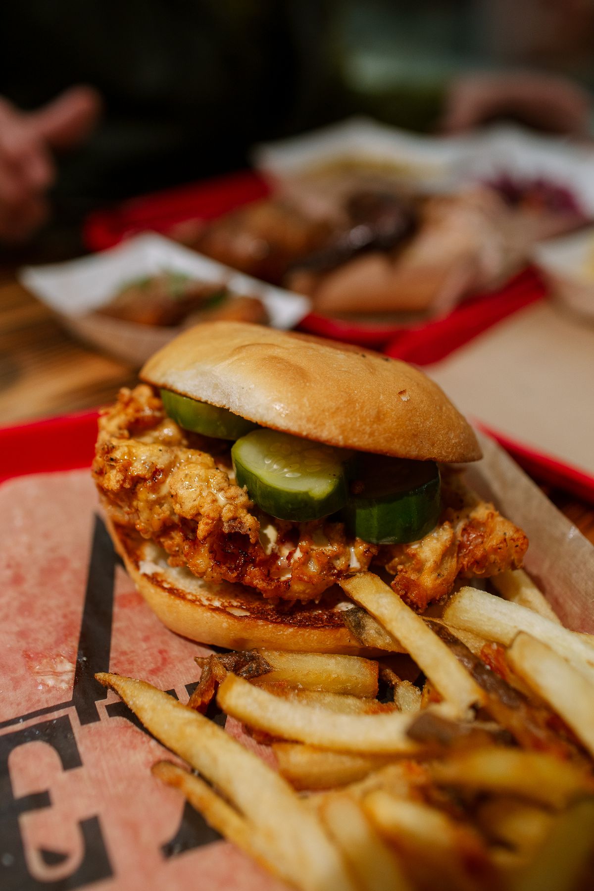 A fried chicken sandwich with homemade pickles is served on a tray with fries.
