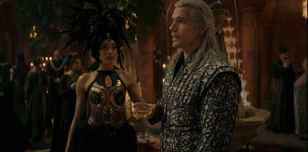 Philippa (Cassie Clare) standing in a flashy feather dress and looking at Geralt (Henry Cavill)