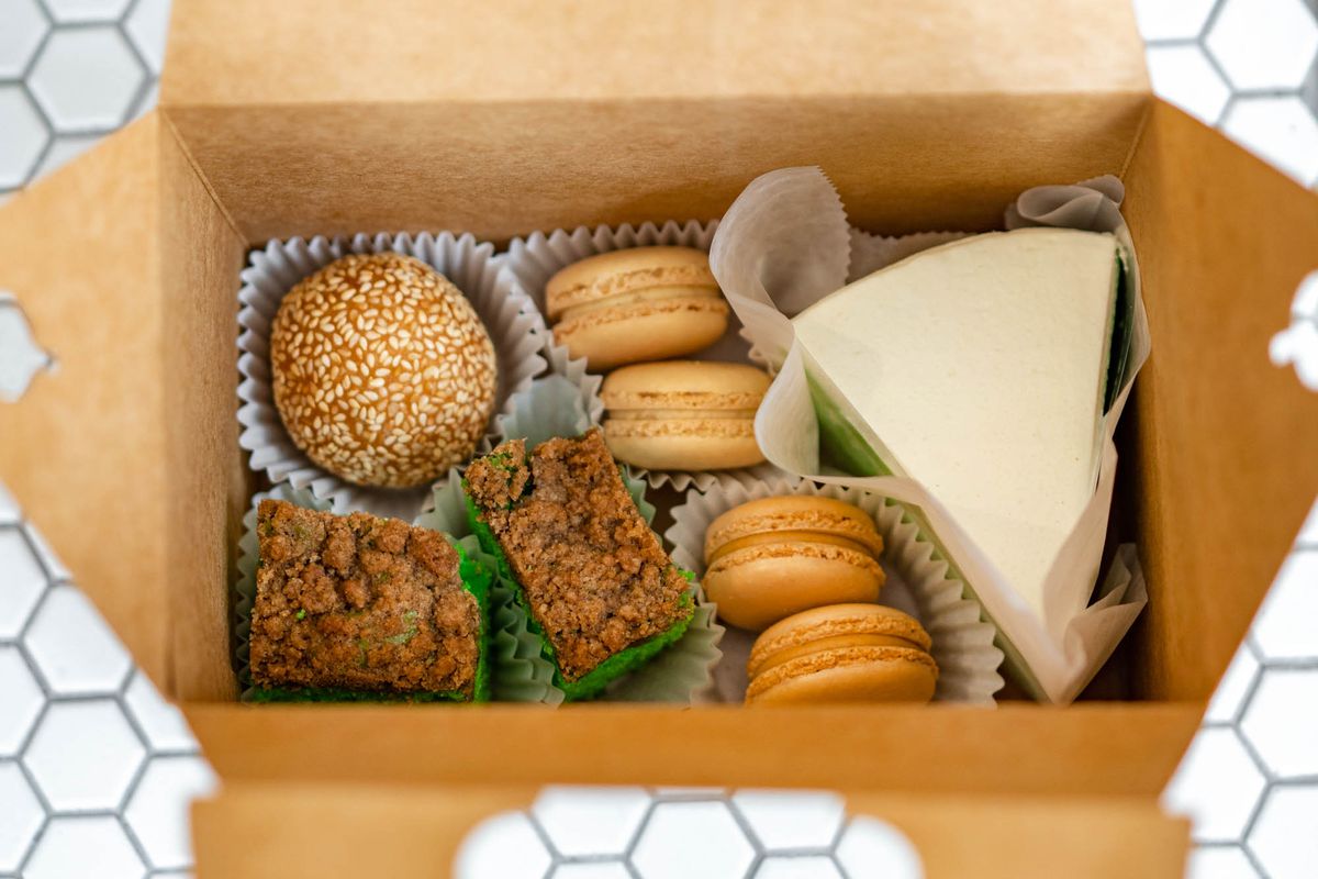 A close-up photo looking into a brown box that is filled with pastries, including a slice of white-frosted cake and four macarons.