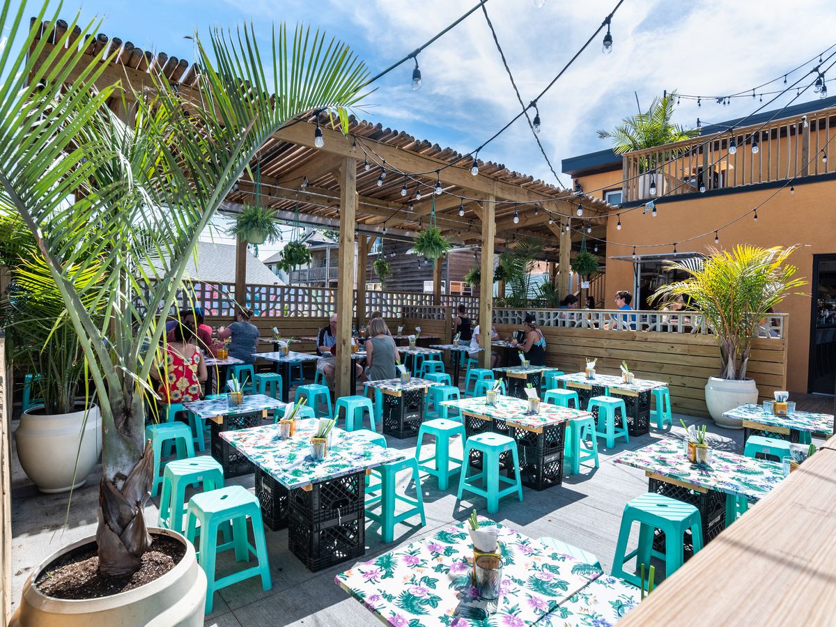 A brightly colored open-air patio with low turquoise stools and oilcloth covered tables