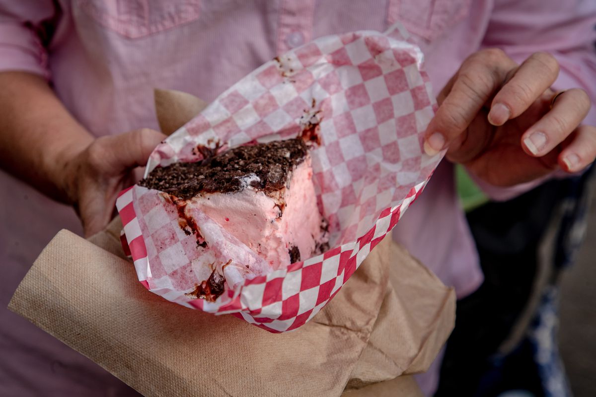 A person holds a peppermint square ice cream dessert in red-and-white checkered wax paper.
