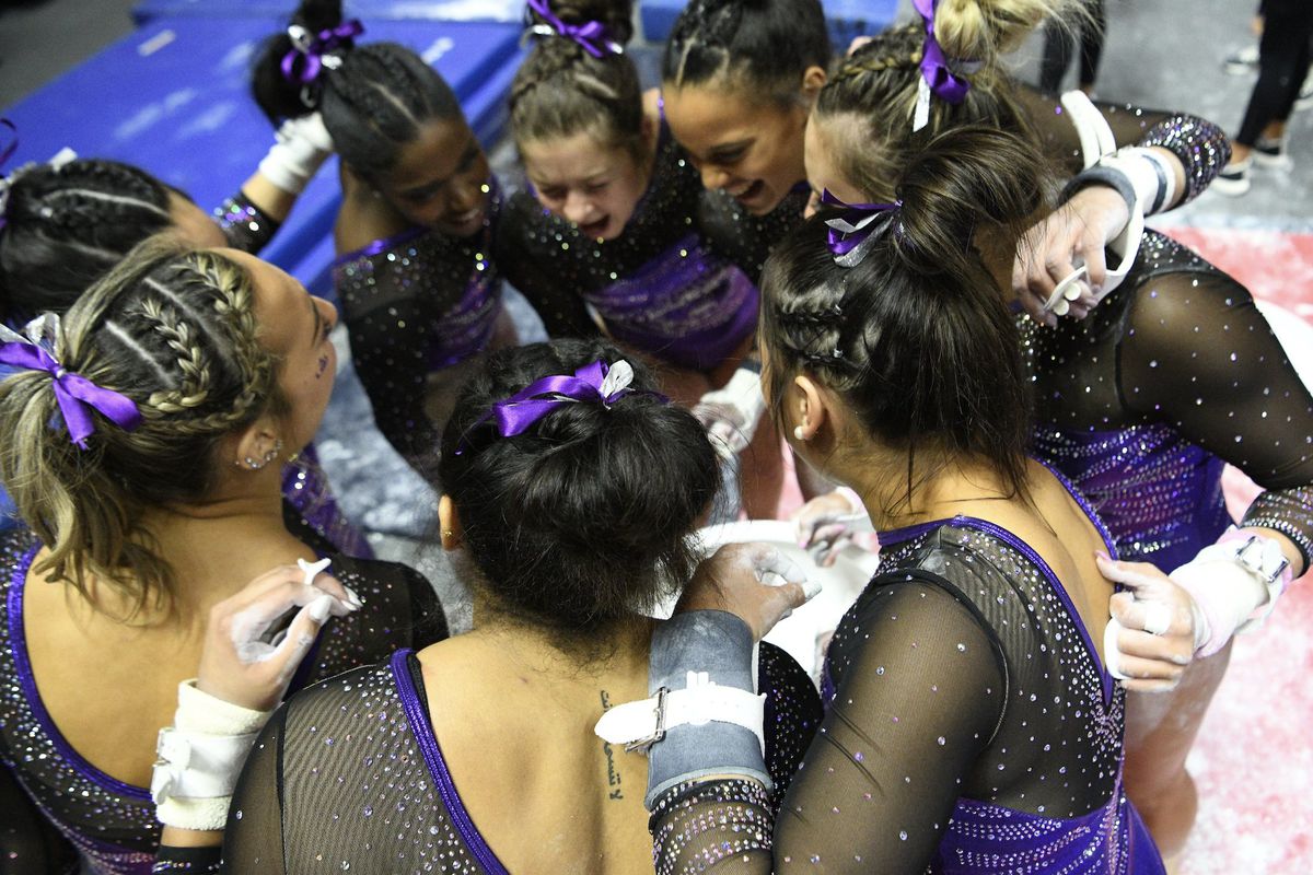 LSU gymnasts stand in a circle wearing competition leotards and bars grips before the first rotation of their meet against Utah Friday