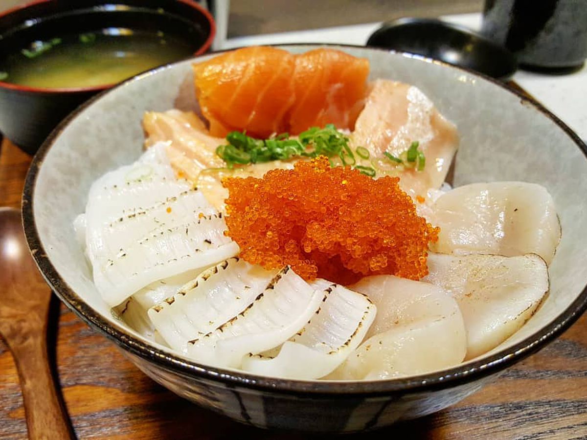 A bowl of raw seafood, including salmon and salmon roe, on rice, served on a wooden tray with miso soup. 