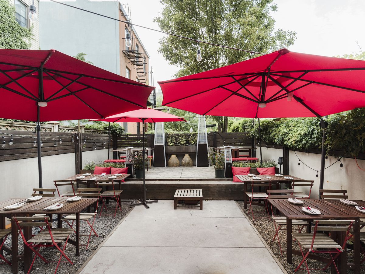 A backyard patio with tables and red umbrellas.