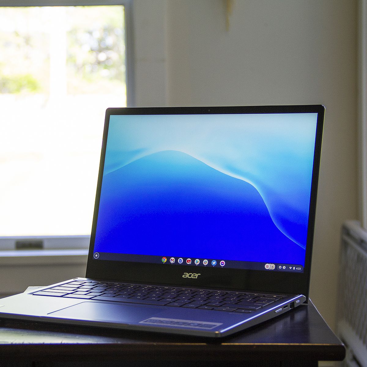 El Acer Chromebook Spin 713 en una mesa pequeña frente a una ventana iluminada.  La pantalla muestra un patrón azul.