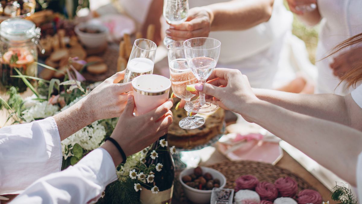 Hands of people wearing white around a picnic table toast with bubbly in glasses. 