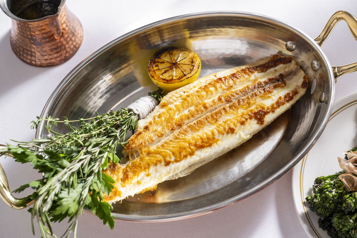 A filet of Dover sole is prestened in a silver tray with a roasted lemon half and a wrapped spring of rosemary and Italian parsley.