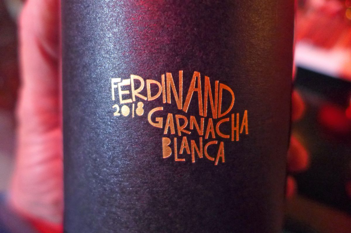 A black bottle of wine with golden lettering held by a fuzzy hand.