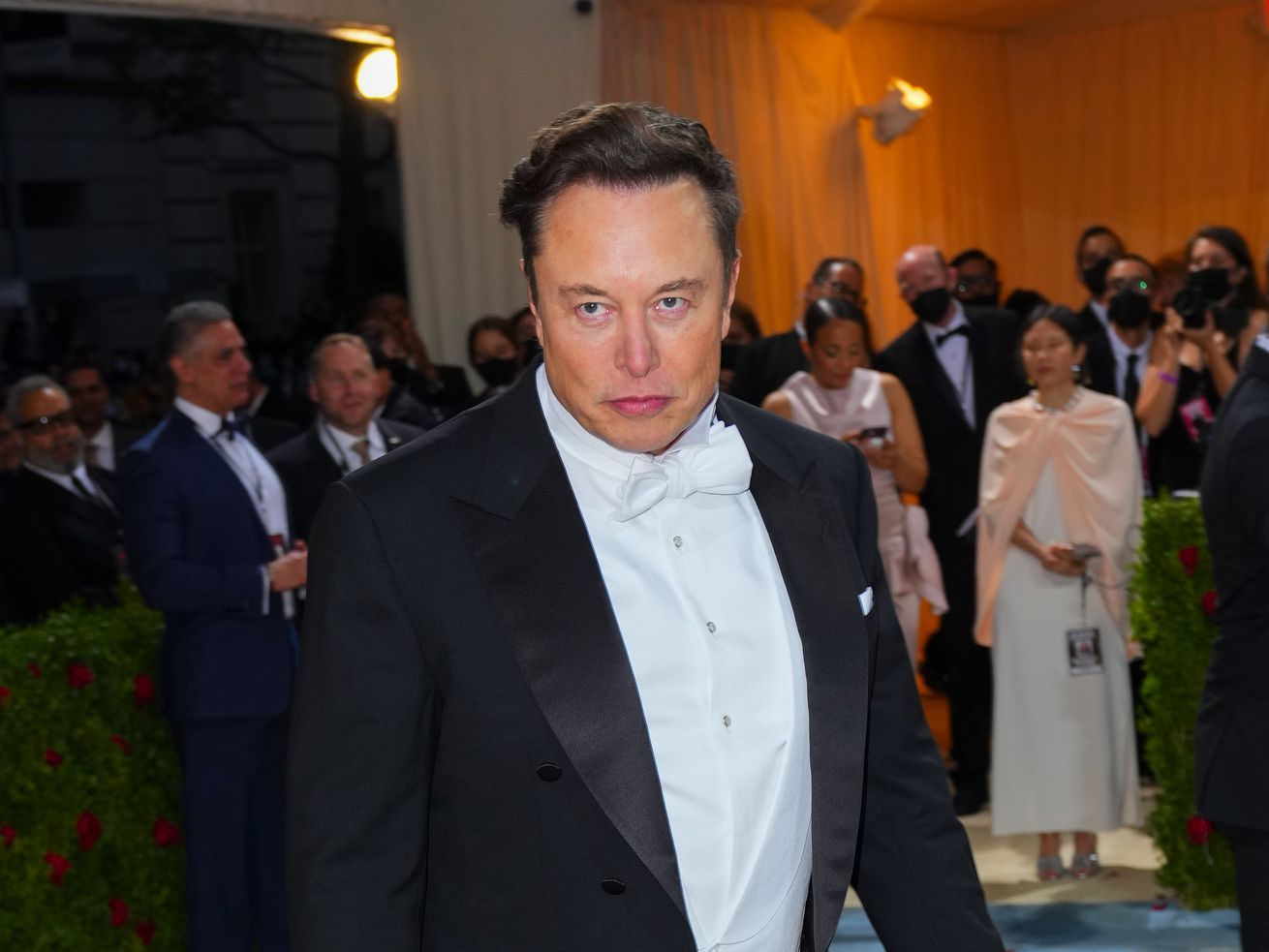 A photo of Elon Musk in a tuxedo from the waist up with a serious expression.