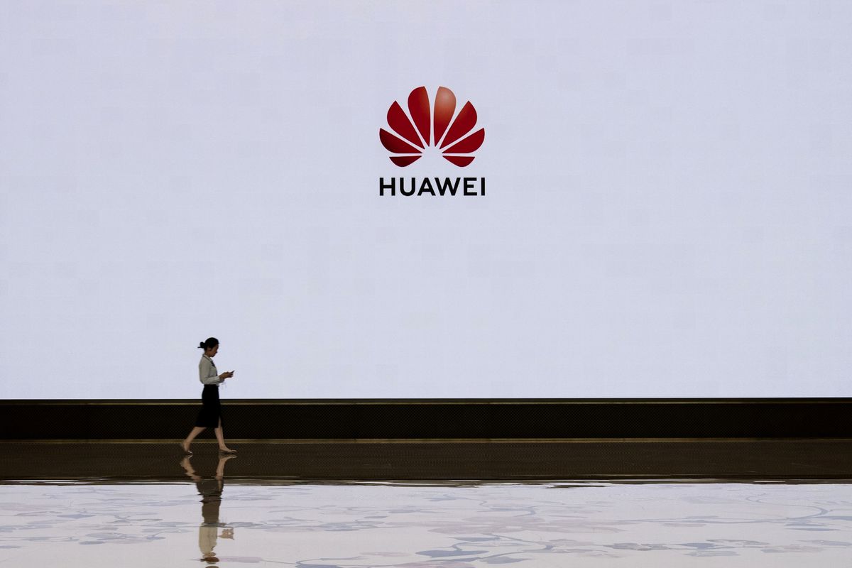 A person walking past a sign reading “Huawei.”