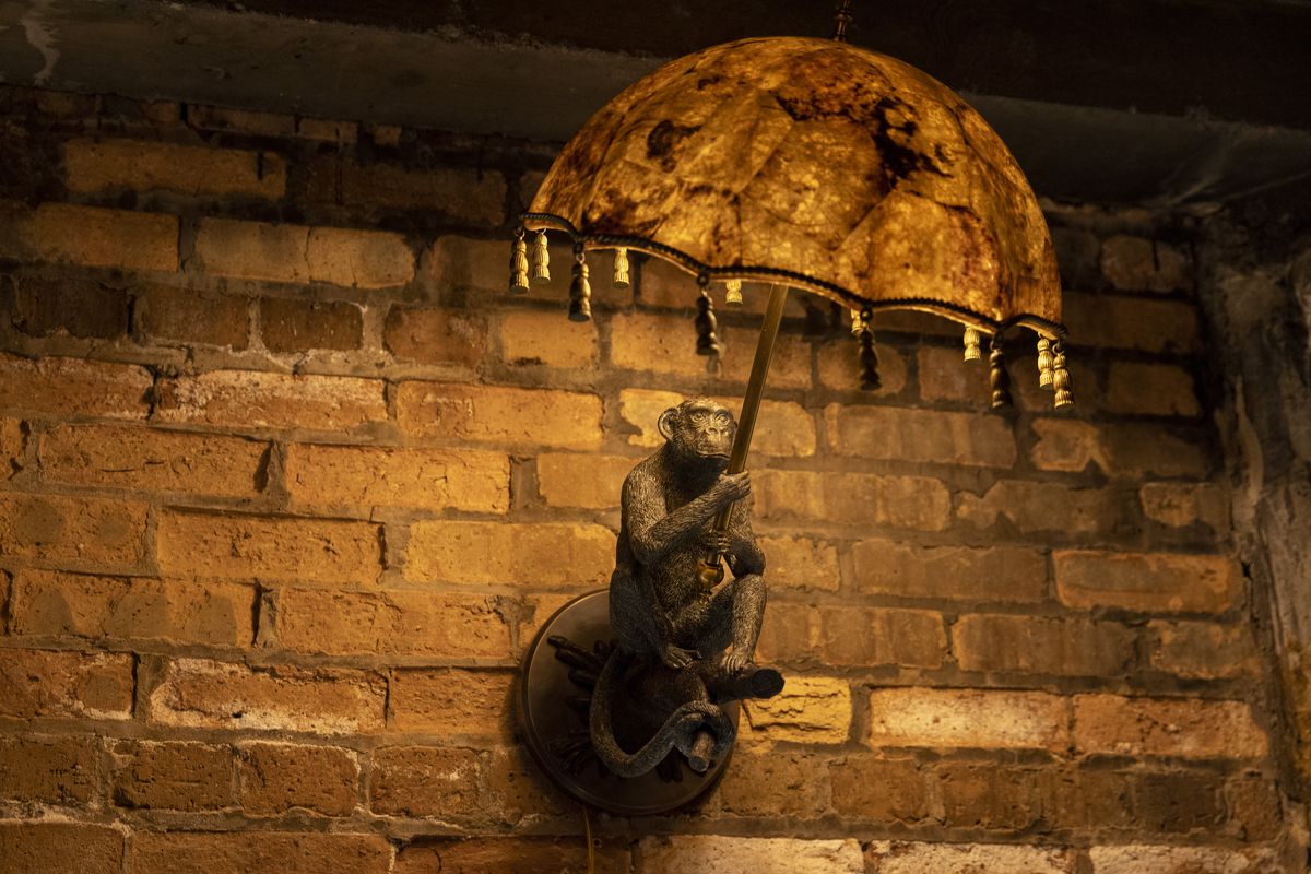 A wall sconce of a metal monkey holding an umbrella-shaped light fixture