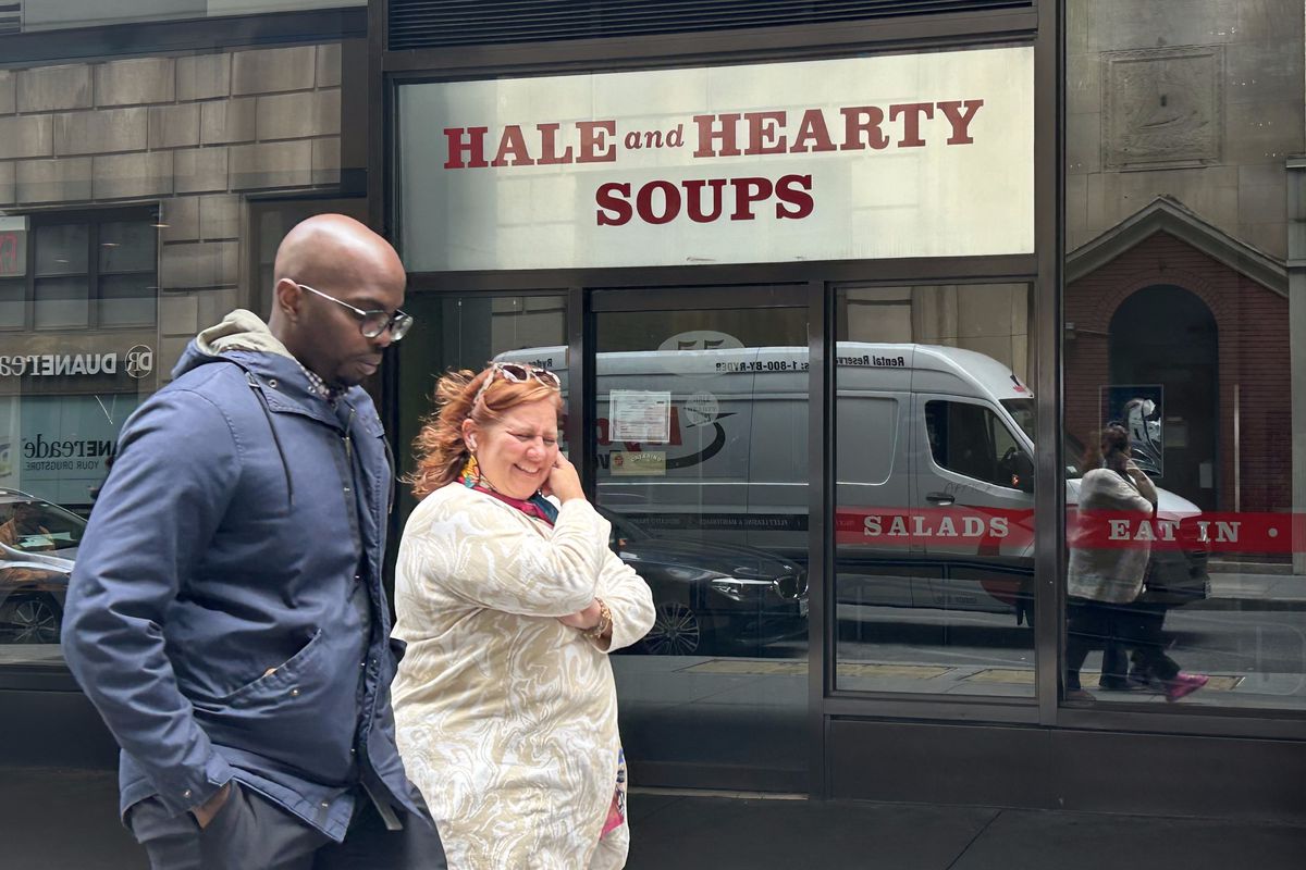 Two people pass in front of a storefront whose sign reads Hale and Hearty soups.