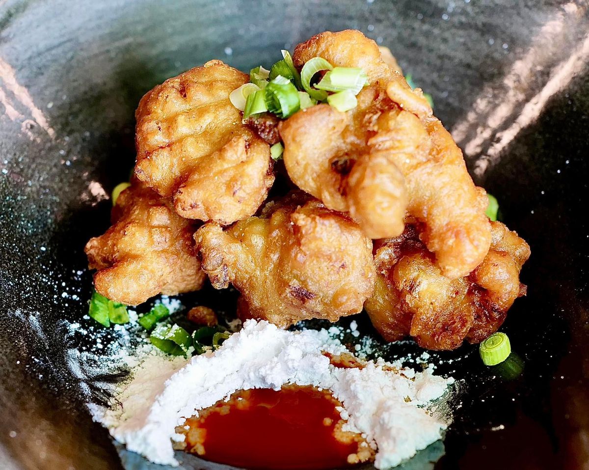 Fried crawfish beignets topped with green onion and plated with powdered sugar and a sauce.