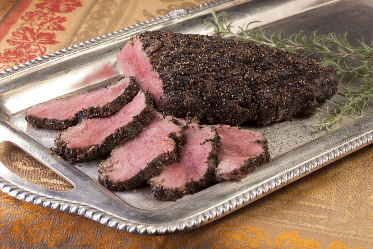 A beef tenderloin sits on a silver platter.