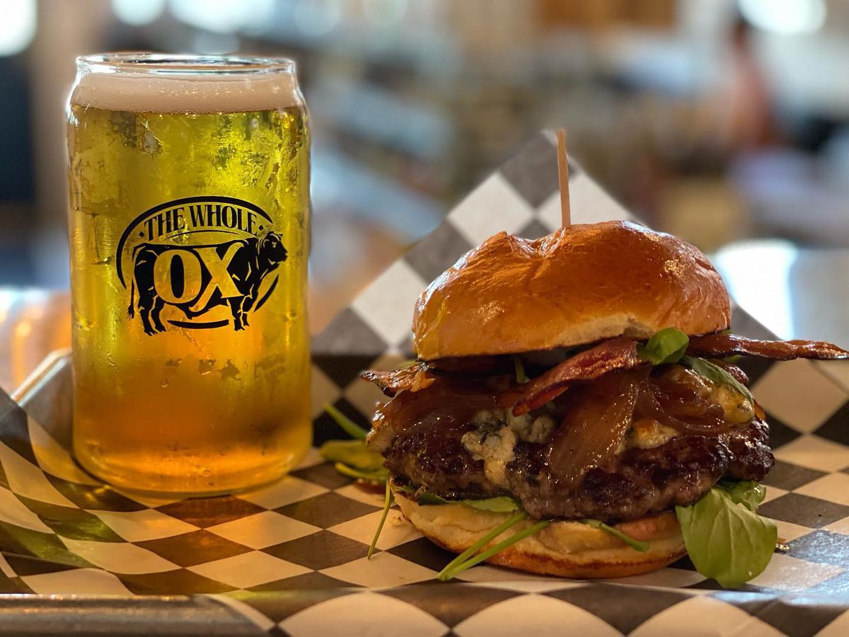 A bison burger with bacon, blue cheese, arugula, garlic aioli, and caramelized onion on a potato bun and draft beer.