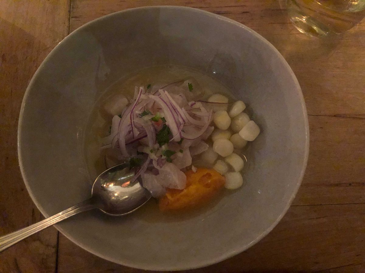 A blue bowl filled with white fish, white corn kernels, red onion shavings, and a dollop of orange sweet potato puree.