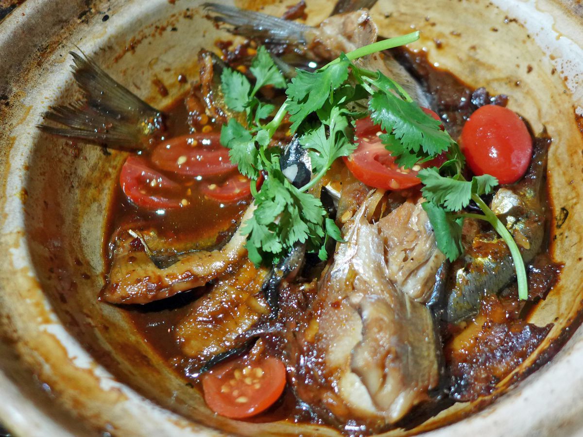 A bowl of sardine fragments in sauce topped with green herbs.