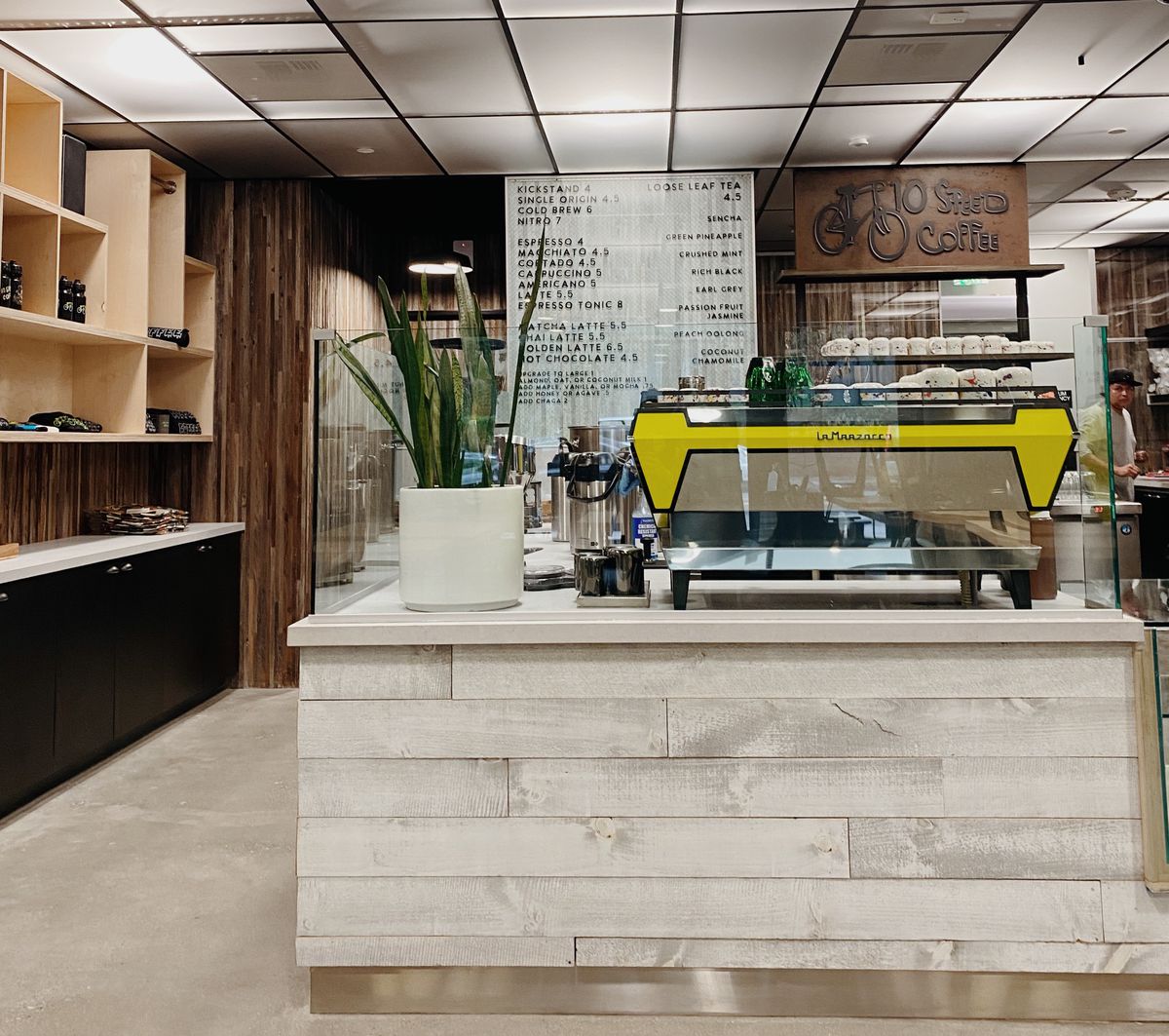 A close up look at a yellow espresso machine inside a grey and tan coffee shop.