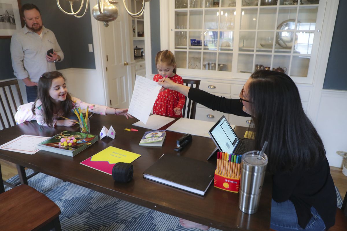 Sarah Yunits checks her daugher Ada's homework while Cora waits her turn as dad Conor Yunits is on a work conference call at their home in Brockton on March 19, 2020. Because of the coronavirus, the Yunits are able to perform their jobs at home and are home schooling their two children.