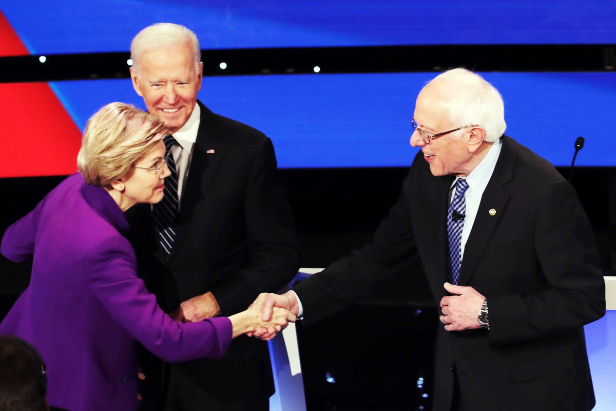 Elizabeth Warren shakes Bernie Sanders’ hand while Joe Biden looks on.