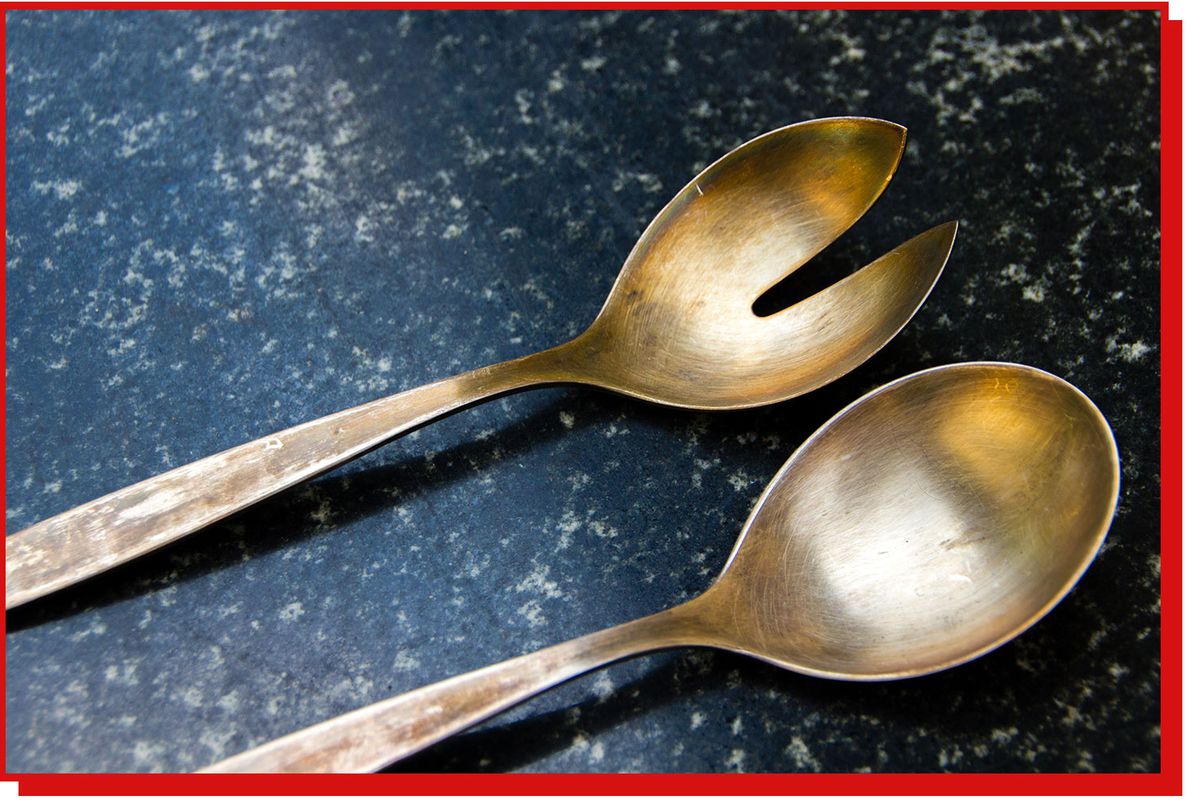 Two golden serving spoons on a marble background.