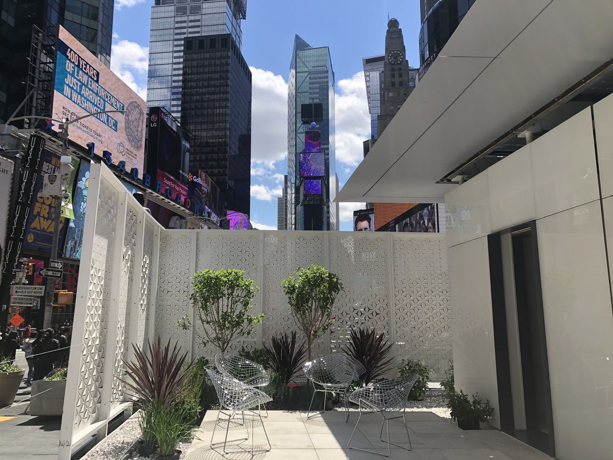 The patio of Futurehaus in Times Square. There are chairs, plants, and a white fence. In the background are the billboards and buildings of Times Square.