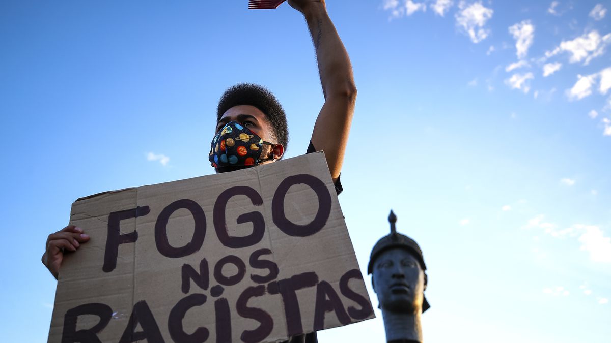 A protester holds a sign that reads, “Fogo now racistas.”