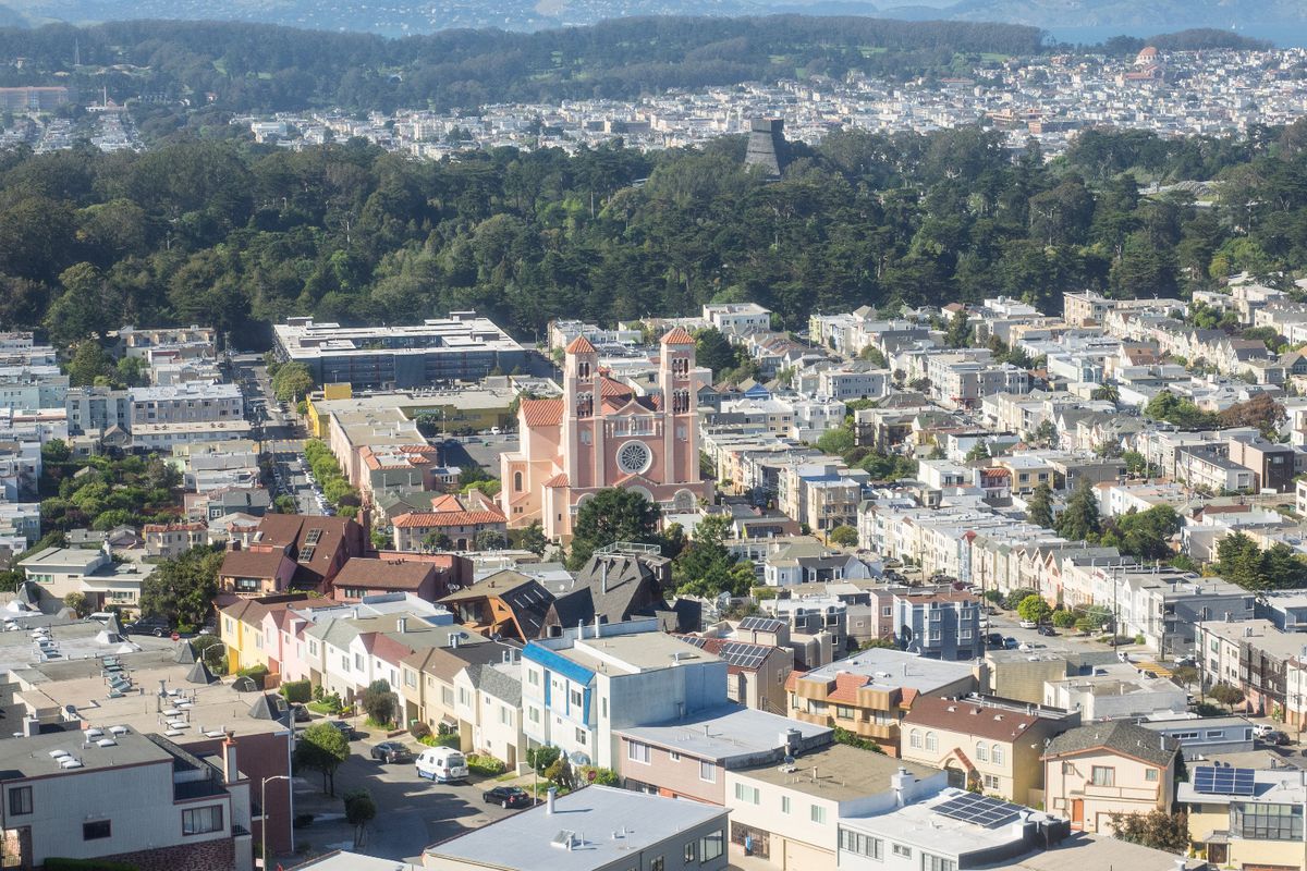 An aerial photo of the Sunset district, facing Golden Gate Park, with the observation deck of the de Young Museum appearing over the trees.