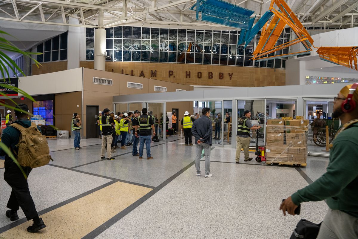 Travelers walk through Houston’s Hobby Airport as construction workers monitor the area.