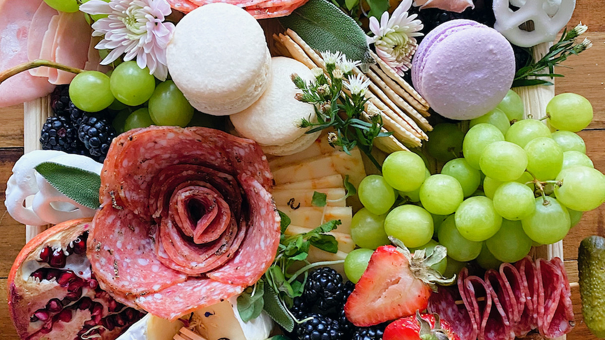 A platter of cheese, grapes, cured meats, crackers, strawberries, and a macaron