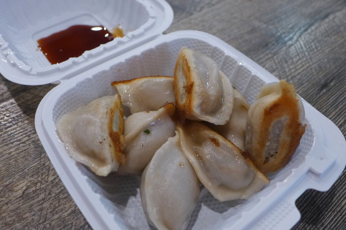 A square white carryout container with humpy dumplings browned on one flat side.