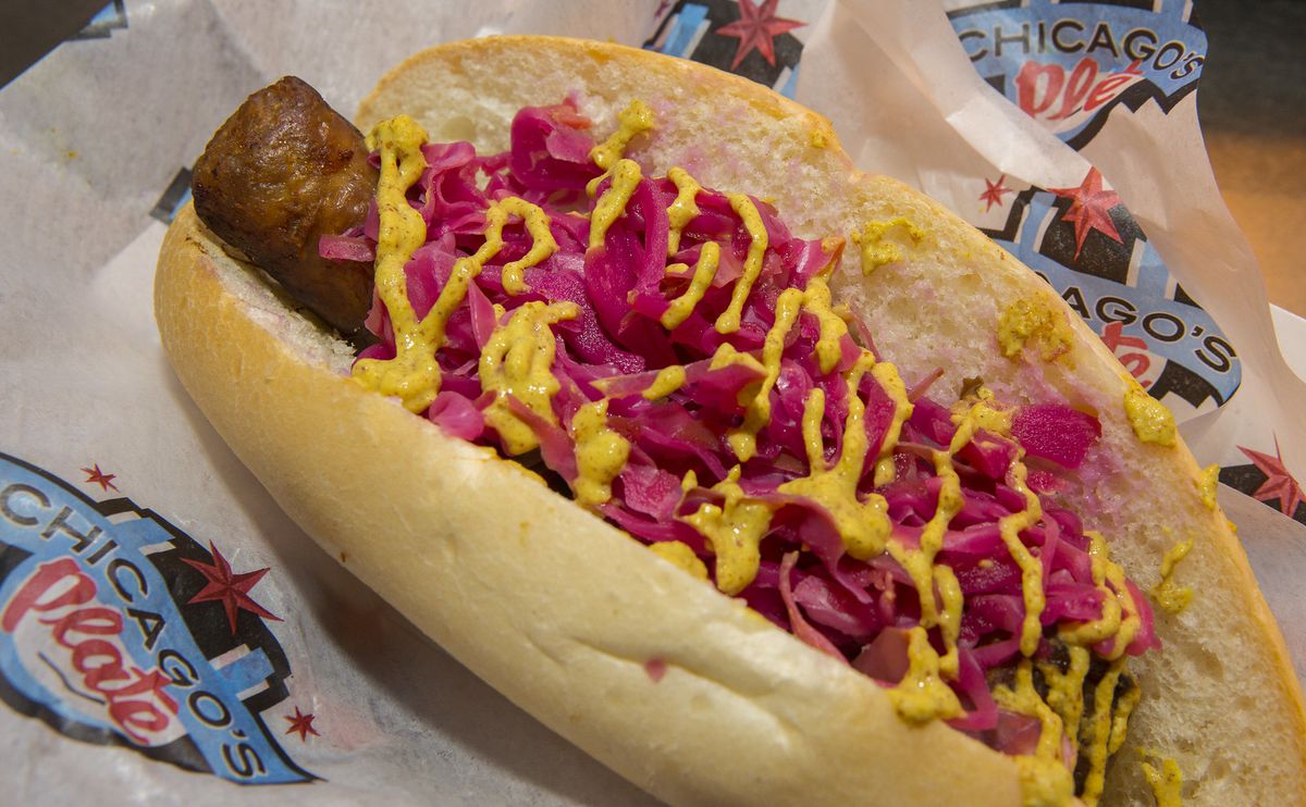 A brat topped with yellow mustard, red cabbage, in between a sausage bun.