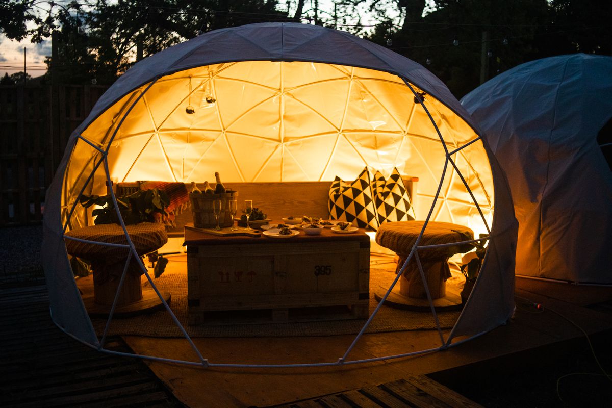 A geodesic dome is half open and filled with furniture. The interior glows at twighlight.