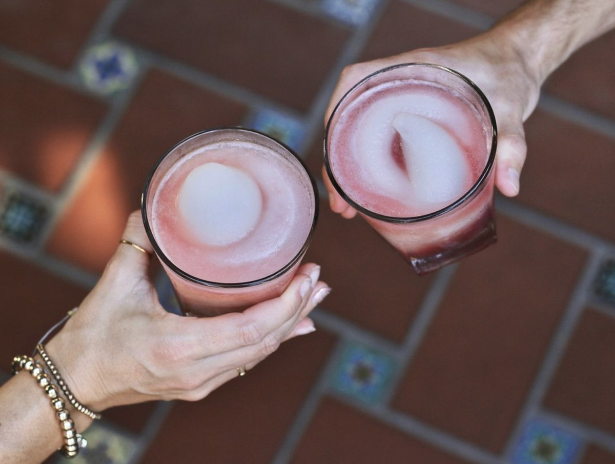 Two people clink together swirled frozen Mambo Taxi margaritas.
