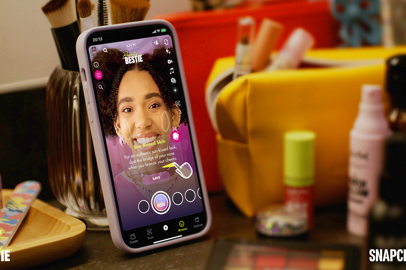 A phone shows a person’s face with a Snapchat makeup filter. The phone is propped up next to makeup products.