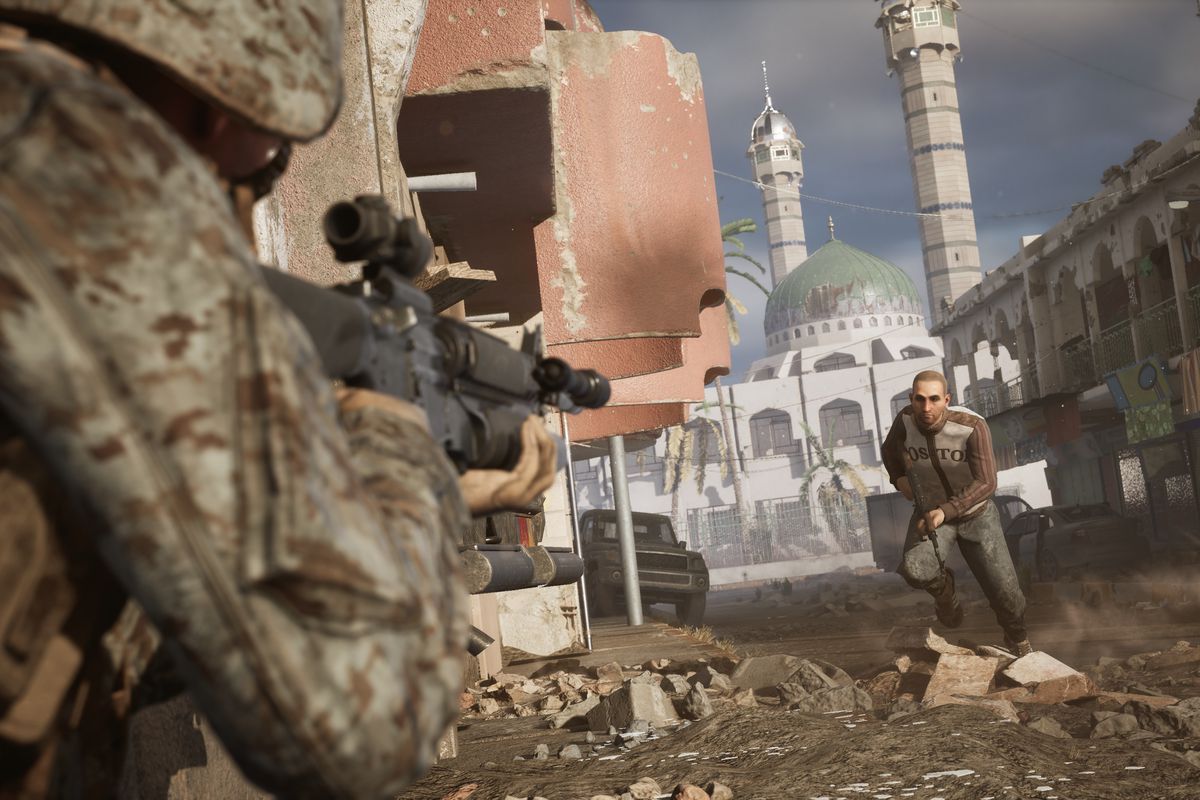 A Marine with a heavily modified weapon takes aim at a man in a rubble-filled street. In the background, a ruined mosque dominates the frame.