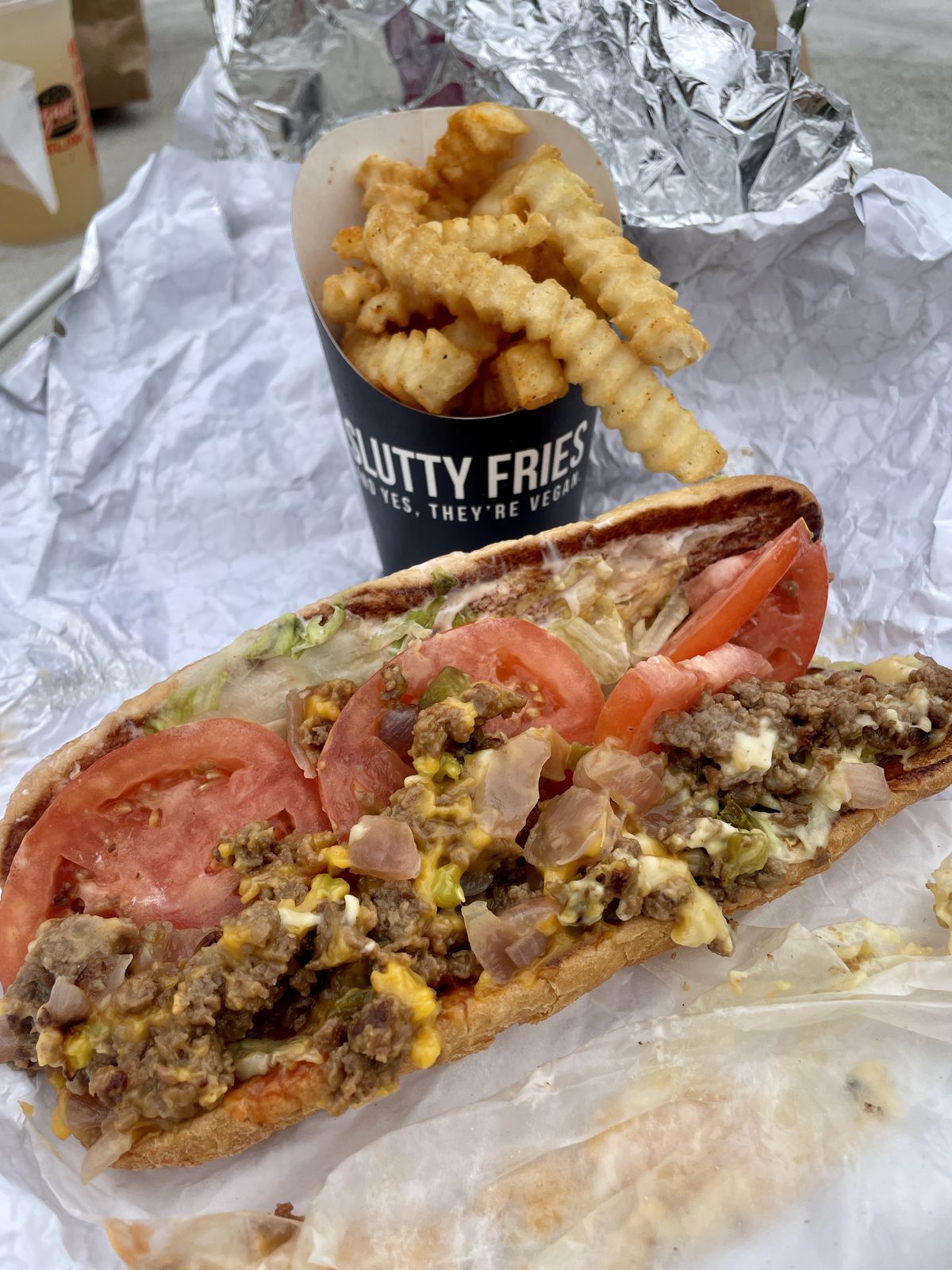 A hoagie sits on foil paper. It’s full of chopped meat, some melted cheese, chopped cheese, tomatoes, and lettuce.
